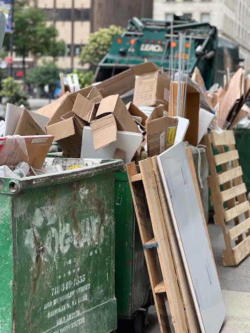 A person wearing a light-colored long-sleeved shirt is disposing of crumpled tissue paper into a cylindrical wooden waste bin positioned against a plain light-colored wall, with their right hand holdi
